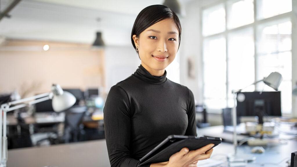 Woman in office holding iPad smiling at the camera